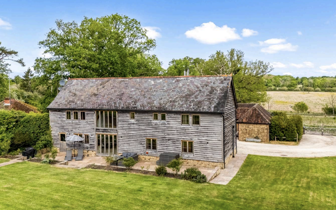 Woodbarn Farm seen from the lawn, with a stone patio, sun loungers and parasol